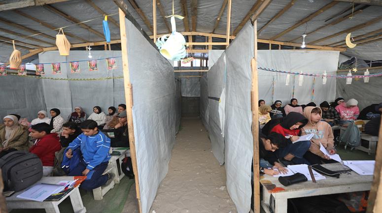 أطفال نازحون يتلقون دروساً داخل خيمة في اليرموك بـغزة، بعد تدمير معظم المدارس وتحويل بعضها لمراكز إيواء بسبب الحرب.