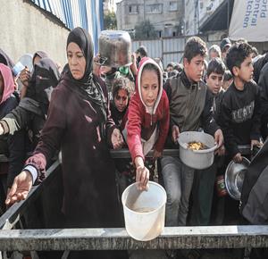 مواطنون يتجمعون في طوابير طويلة لتلقي وجبات ساخنة من تكية خيرية في مخيم النصيرات، وسط قطاع غزة