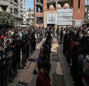 مواطنون يؤدون صلاة الجمعة الثالثة من شهر رمضان بين أنقاض مسجد الفاروق الذي دُمّر جراء الغارات الإسرائيلية خلال الحرب، في مخيم النصيرات وسط قطاع غزة