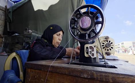 مسنّة تواصل حياكة الملابس في خيمة النزوح 